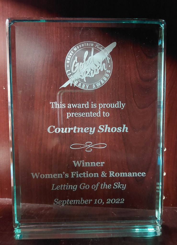 A glass award plaque with text etched on it saying "This award is proudly presented to Courtney Shosh, winner, Women's Fiction & Romance, Letting Go of the Sky, September 10, 2022."